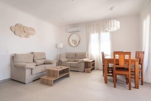 Ein modernes Wohnzimmer mit Sofa, Couchtisch, Esstisch mit Stühlen und einer Pendelleuchte.