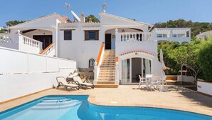 Una villa blanca con piscina, mobiliario de exterior y una escalera que lleva a la entrada.