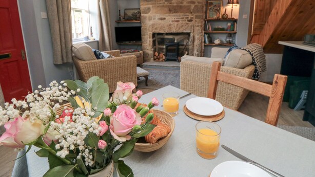 Ein gemütliches Wohnzimmer mit Korbmöbeln, einem Kamin aus Stein und einem Esstisch, der mit Blumen und Orangensaft gedeckt ist.