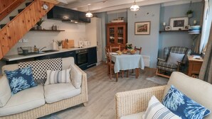 Ein gemütliches Wohnzimmer mit einer Couch und Sesseln, einem Esstisch mit Stühlen, einer Küchenzeile mit Herd und Schränken sowie einer Treppe.