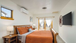 A bedroom with a wooden bed, a nightstand, a lamp, a TV, and a window with curtains. - Hazel @ Stella Ruby Cottages - Steps to Downtown (Moab)