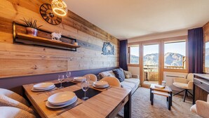 A cozy room with a wooden wall, a dining table set with plates and glasses, a sofa, and a view of mountains through large windows. - Immodreams - La Fruitière - Avoriaz (Avoriaz)