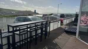 Terraza con mobiliario exterior, con vistas a un estacionamiento y al mar.