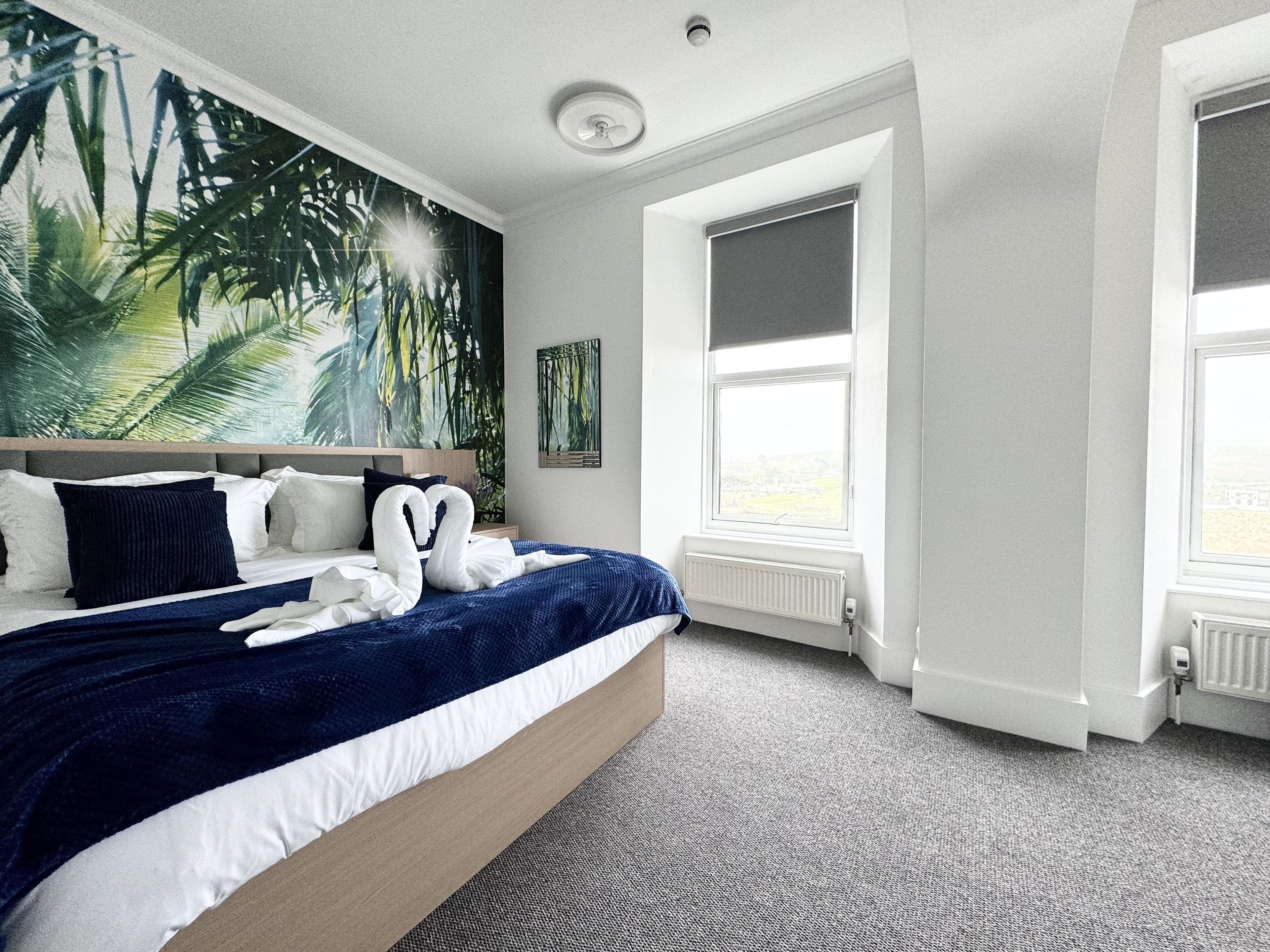 A hotel room with a large bed, a headboard, a wall mural, a window, and a radiator.
