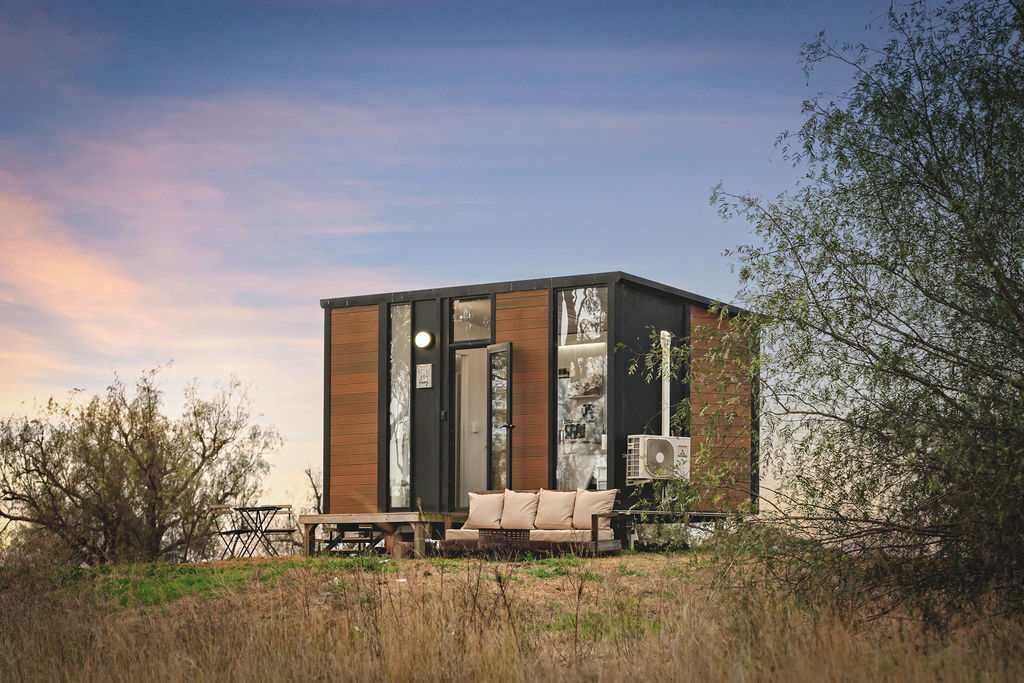 A modern, cube-shaped building with large windows, a wooden exterior, and a seating area with a sofa and table.