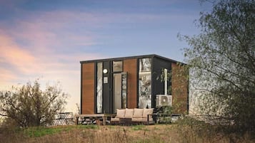 A modern, cube-shaped building with large windows, a wooden exterior, and a seating area with a sofa and table.