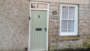 Un edificio de piedra con una puerta verde y una ventana con cortinas de encaje. Un letrero dice 'Bay Tree Cottage 15 Westgate'.