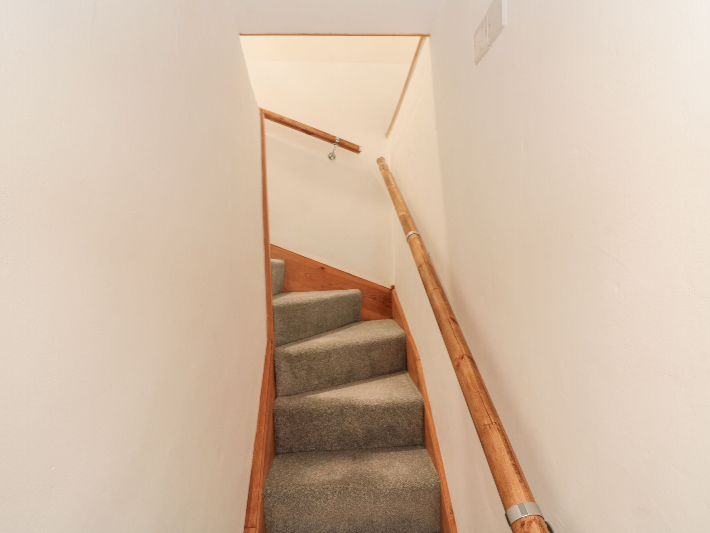 Un escalier étroit avec des rampes en bois et des marches recouvertes de moquette.
