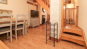 Una sala de estar acogedora con una escalera de madera, un comedor con sillas y una mesa, y un televisor sobre un mueble.