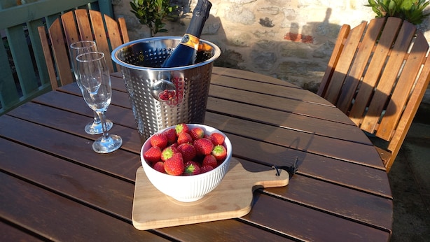 Una mesa de madera con un bol de fresas, un recipiente de metal con una botella y dos copas de vino vacías.