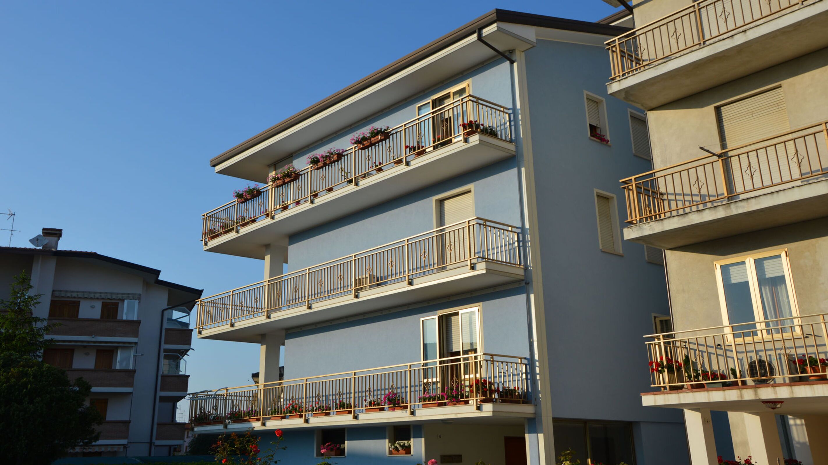 A multi-story residential building with balconies, each adorned with potted plants.