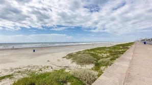 A beach with a concrete walkway, grassy areas, and a clear sky with clouds. - Paradise Found! Stop Looking! (Galveston)