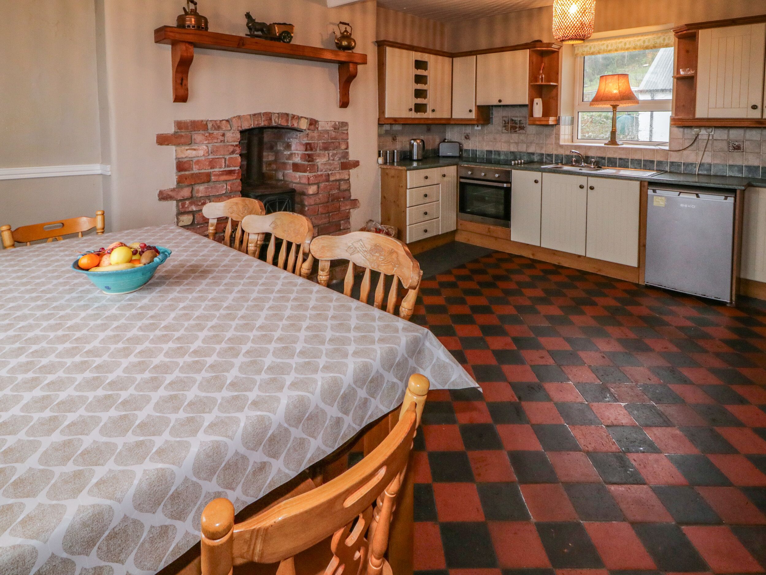 A kitchen with a brick fireplace, wooden cabinets, a dining table with chairs, and a checkered floor.