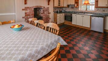 A kitchen with a brick fireplace, wooden cabinets, a dining table with chairs, and a checkered floor.