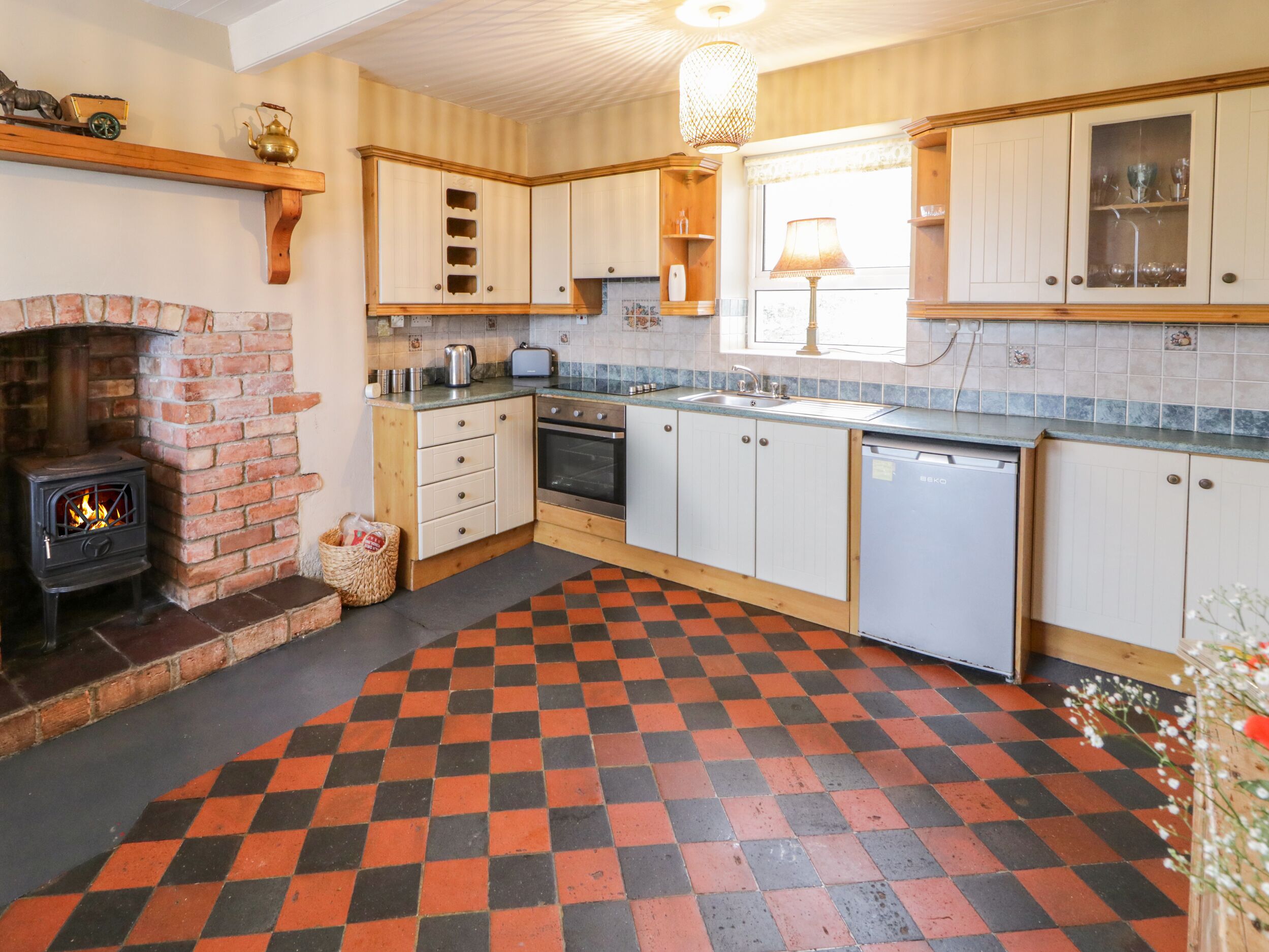 A kitchen with a brick fireplace, wooden cabinets, a checkered floor, and a dishwasher.