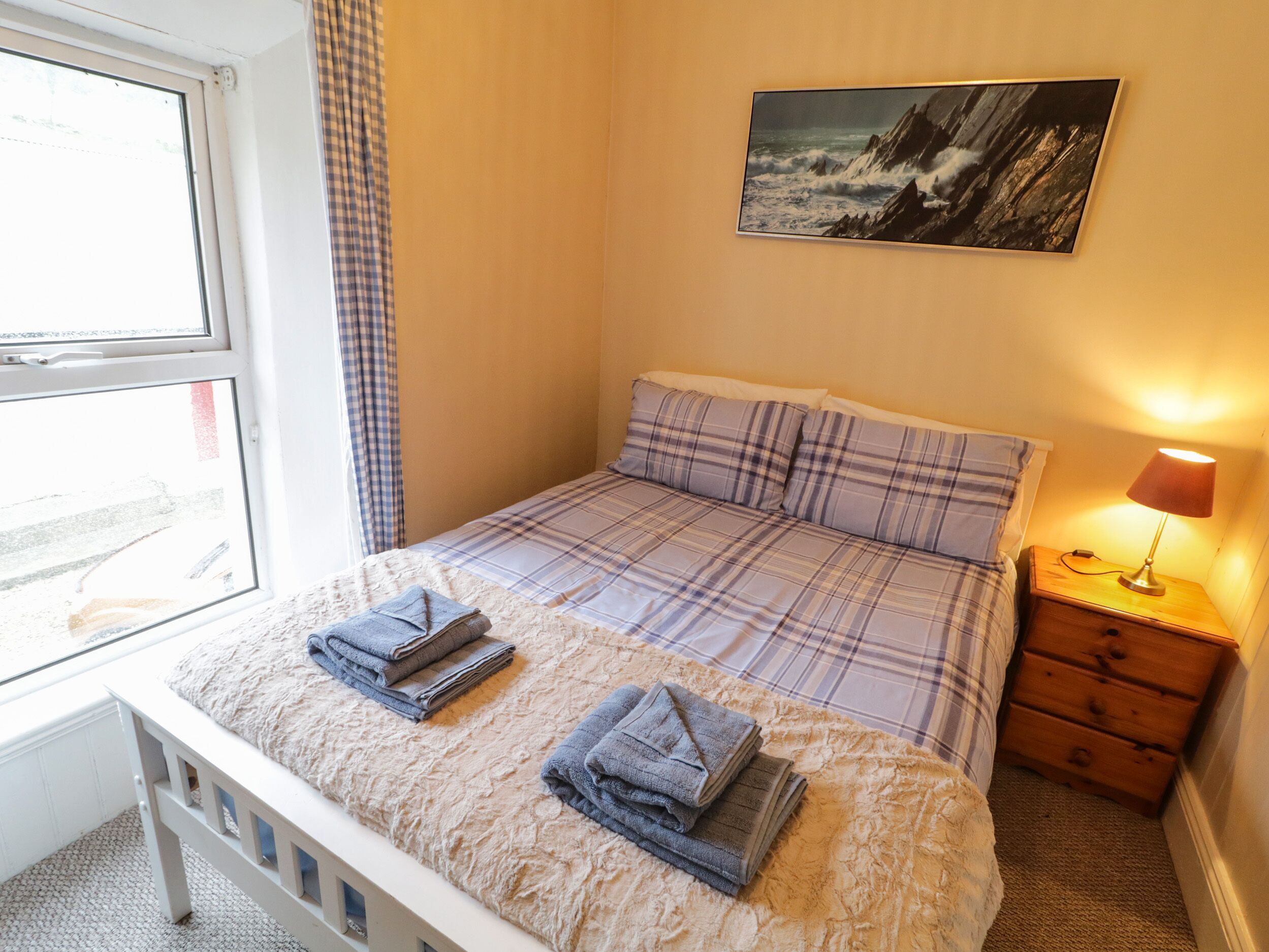 Una camera da letto con un letto, un comodino, una lampada, una finestra e un quadro appeso al muro.