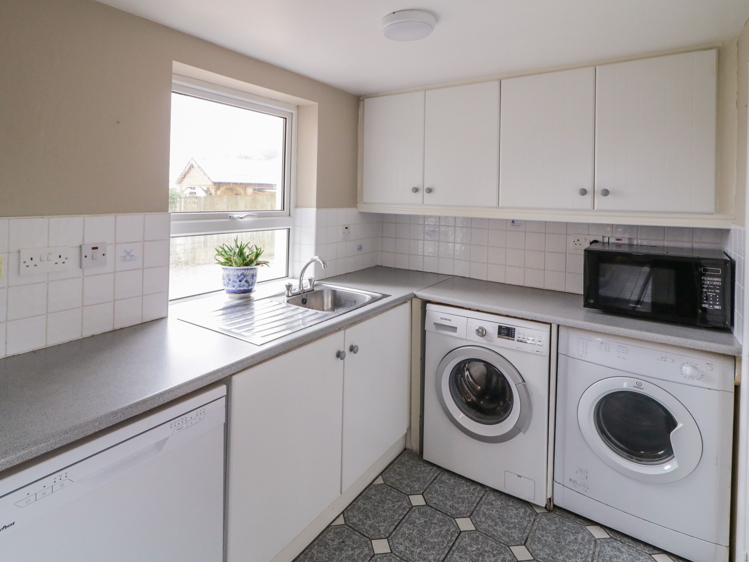A compact kitchen with white cabinets, a washing machine, a microwave, and a sink.