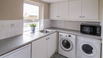 A compact kitchen with white cabinets, a washing machine, a microwave, and a sink.