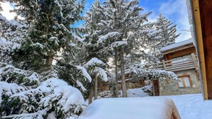 A wooden deck covered in snow, surrounded by snow-covered trees and a stone building.