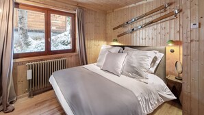 A wooden cabin bedroom with a bed, window, ski rack, and a radiator.