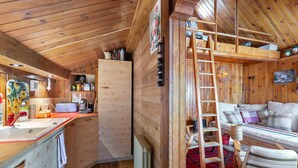 A cozy cabin interior with a kitchen area, a wooden ladder, a sofa, and a plaid rug.