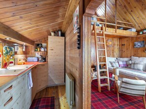 A cozy cabin interior with a kitchen area, a wooden ladder, a sofa, and a plaid rug.