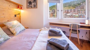 Ein Schlafzimmer mit Bett, Schreibtisch und Blick auf eine Stadtlandschaft durch ein Fenster.