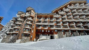 Ein mehrstöckiges Hotel mit Balkonen, einer Stein-Fassade und einer Skipiste im Vordergrund.
