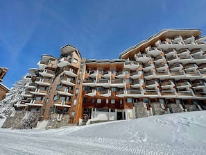 Un hôtel à plusieurs étages, doté de balcons et d’une façade en pierre, avec une piste de ski en premier plan.