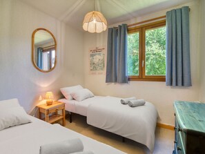 A bedroom with two beds, a bedside table with a lamp, a mirror, a window with curtains, and a poster on the wall.