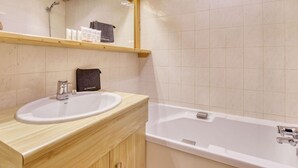A bathroom with a wooden vanity, a white sink, a bathtub, and a shelf with toiletries. - Charming ski-in apartment in Courchevel with parking included (La Tania)
