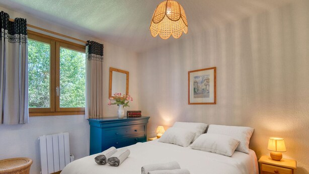 A bedroom with a bed, bedside tables, a dresser, a window, and a hanging light fixture. - Charming ski-in apartment in Courchevel with parking included (La Tania)