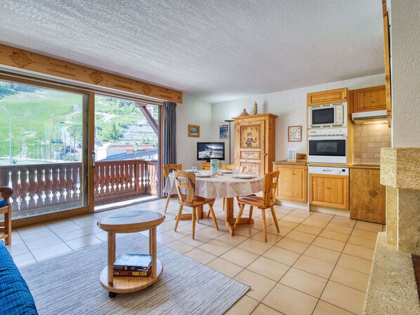 A dining area with a table and chairs, a kitchen with wooden cabinets, and a view through a glass door.