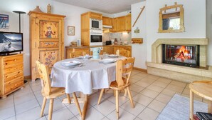A dining area with a round table, wooden chairs, a fireplace, and a kitchen in the background. - Charming ski-in apartment in Courchevel with parking included (La Tania)