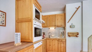 A kitchen with wooden cabinets, a white stove, and a tiled backsplash. - Charming ski-in apartment in Courchevel with parking included (La Tania)
