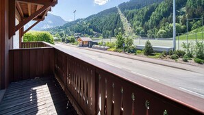 A wooden balcony with a view of a road, greenery, and mountains. - Charming ski-in apartment in Courchevel with parking included (La Tania)