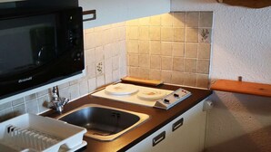 A compact kitchen with a Brandt microwave, a sink, and a countertop with a cutting board.