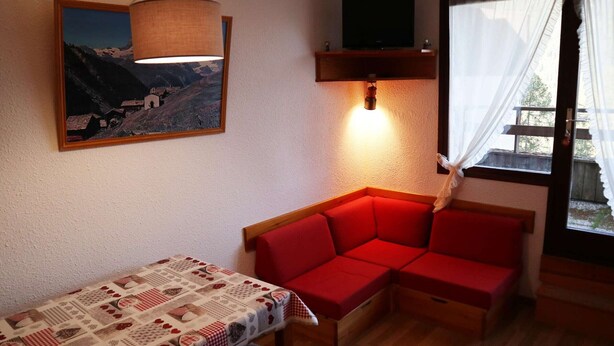 A cozy room with a wooden table, red sofa, a mounted TV, and a painting.