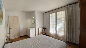 Ein Schlafzimmer mit Bett, Fenster mit Vorhängen, Heizkörper, Stuhl und Kleiderschrank.