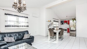 A modern living room with a leather sofa, a glass coffee table, and a chandelier. There is a dining area with a white table and chairs, and a kitchen with red cabinets and a stainless steel refrigerator. - 3 bedroom awesome apartment in Vir (Vir)