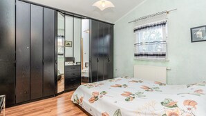 A bedroom with a wooden floor, a bed with a floral bedspread, a wardrobe, a radiator, and a window with curtains. - 3 bedroom awesome apartment in Vir (Vir)