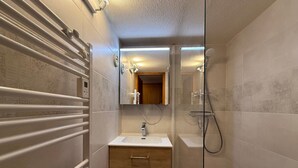 Un baño moderno con cabina de ducha de vidrio, tocador de madera con lavamanos y espejo sobre el tocador.
