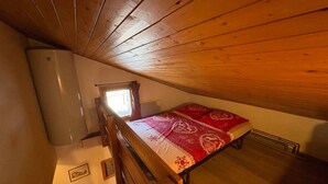 Un dormitorio en el ático, pequeño, con techo inclinado, una cama individual con colcha estampada, una ventana con cortinas y un radiador.