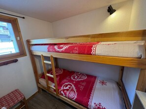 Una cama litera con ropa de cama roja y blanca, una escalera de madera, una ventana con vistas y un pequeño banco.
