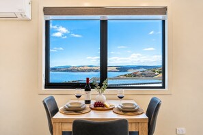 Een eettafel met uitzicht op een kustlandschap door een groot raam.