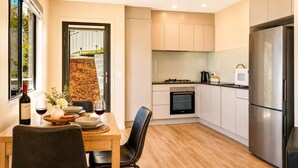 A modern kitchen with a dining area, featuring a built-in oven, a stainless steel refrigerator, and a window overlooking a garden. - View Studio | Derwent River Views | Sandy Bay (Sandy Bay)