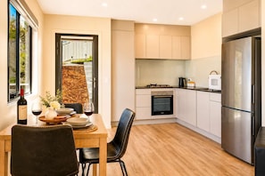 Een moderne keuken met een eethoek, met een inbouwoven, een roestvrijstalen koelkast en een raam met uitzicht op een tuin.