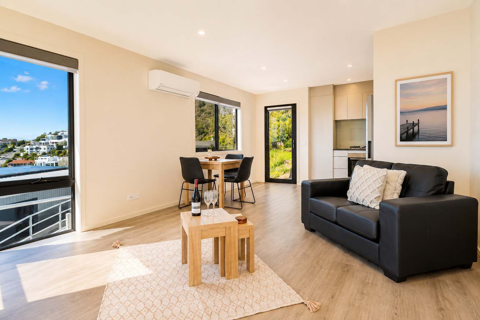 Uma sala de estar moderna com um sofá preto, uma mesa de jantar com cadeiras e vista para o exterior.
