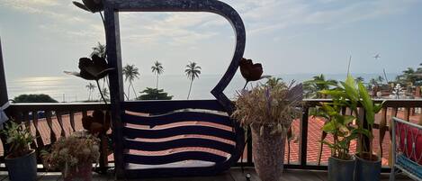 A wooden deck with a large decorative planter, potted plants, and a view of the ocean.