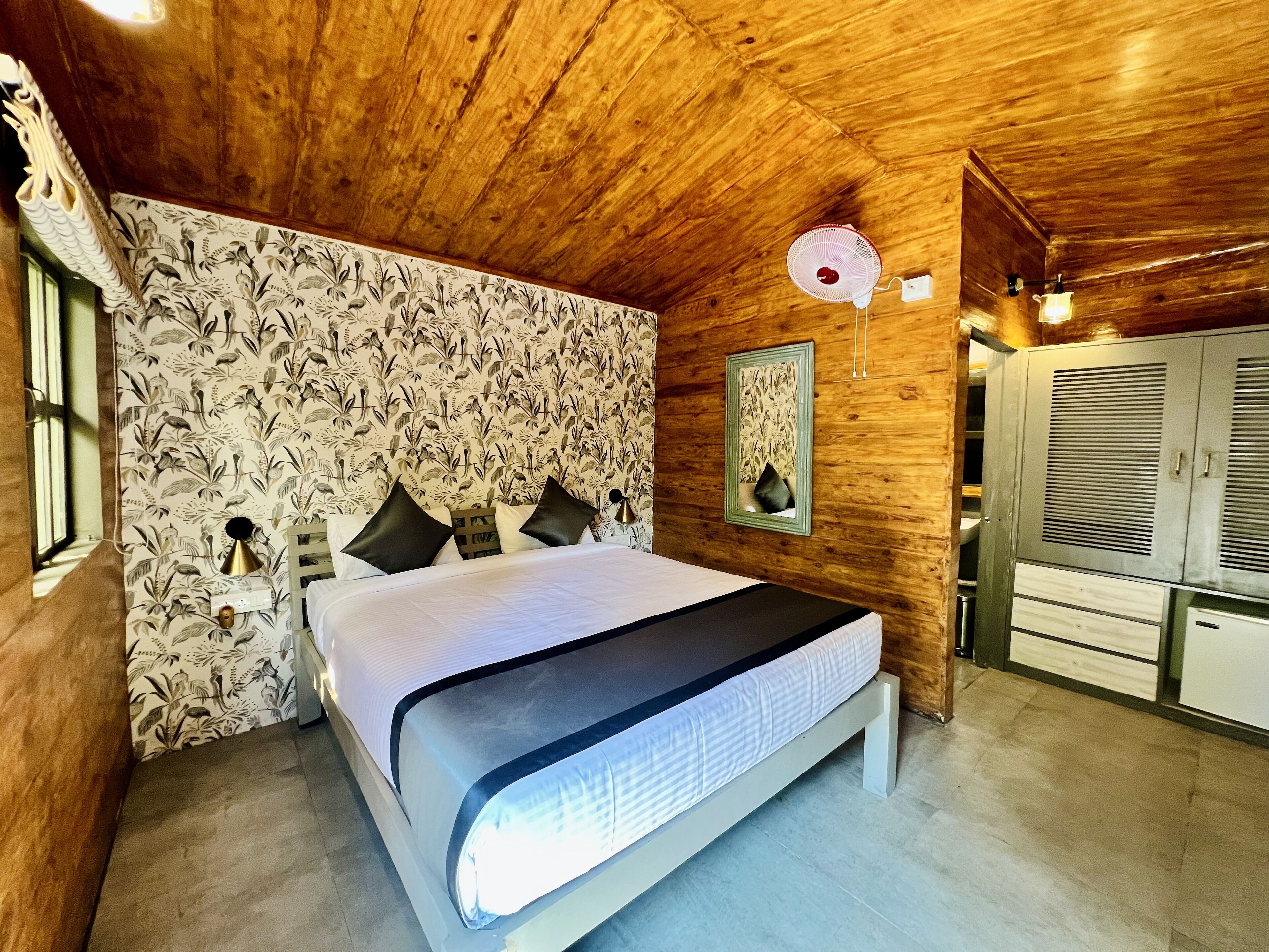 Un dormitorio con techo de madera, una cama con ropa de cama blanca, una mesita de noche, un espejo montado en la pared y un armario.